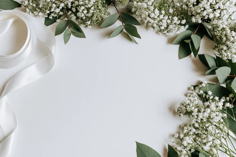 Baby's-breath and eucalyptus arranged in a flat lay with white ribbon on a white surface, forming a decorative border with copyspace in the center