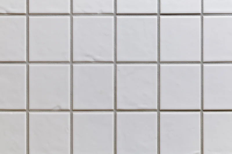 White ceramic tiles arranged in a grid pattern covering a wall surface