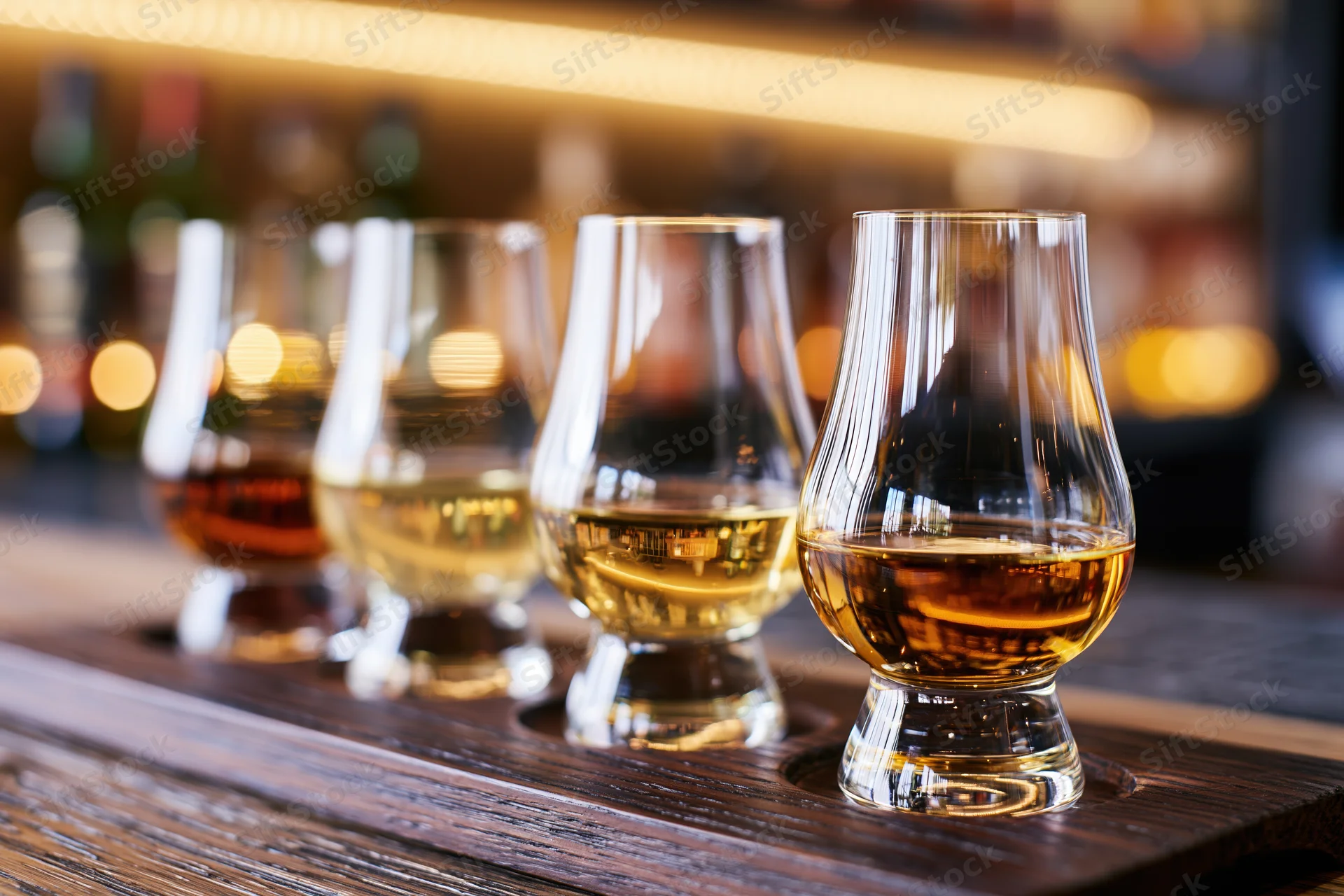 Four glencairn whisky glasses arranged in a tasting flight on a wooden tray at a bar