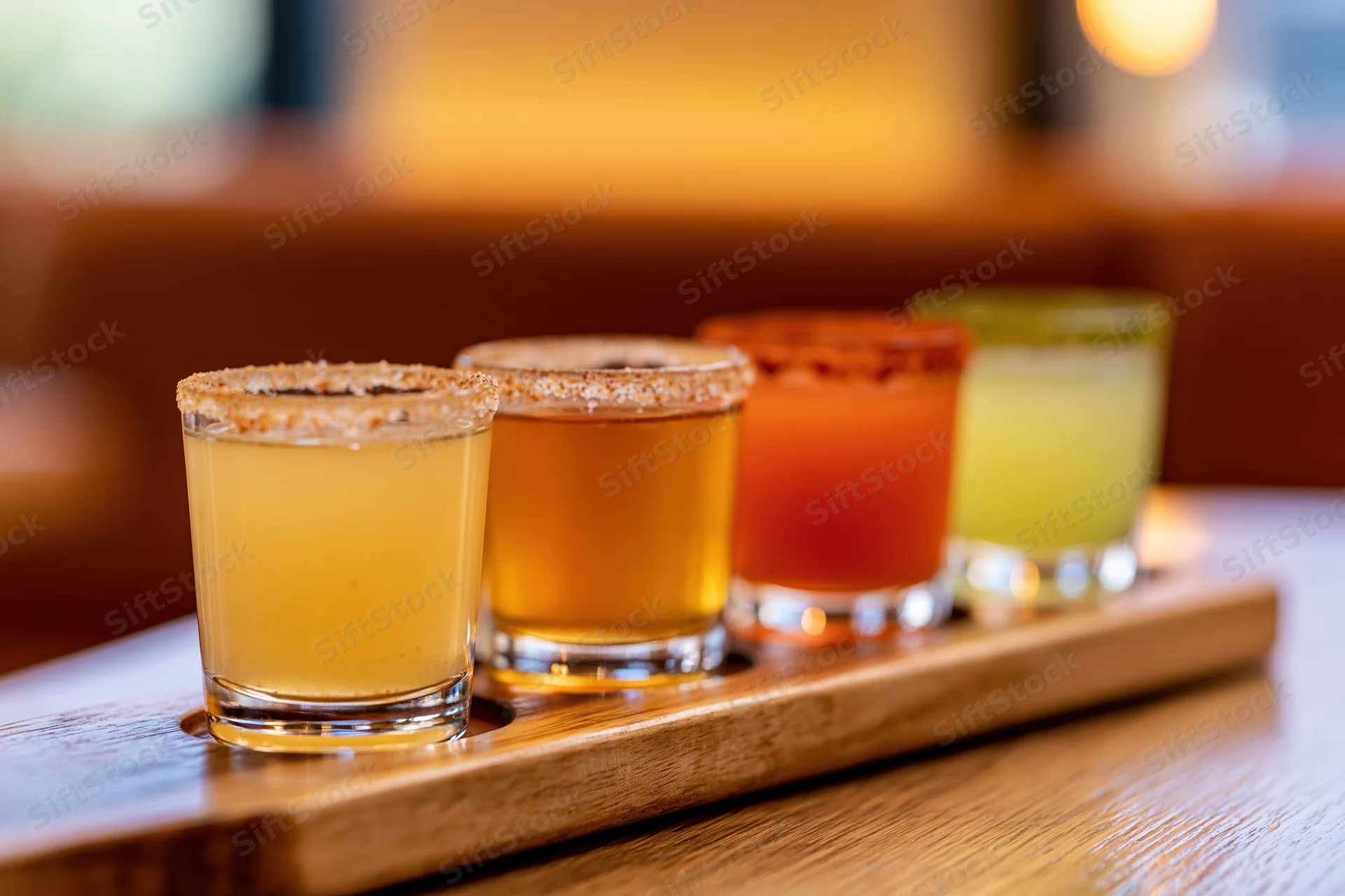Four margarita flight glasses arranged in a row on a wooden tray in a bar setting