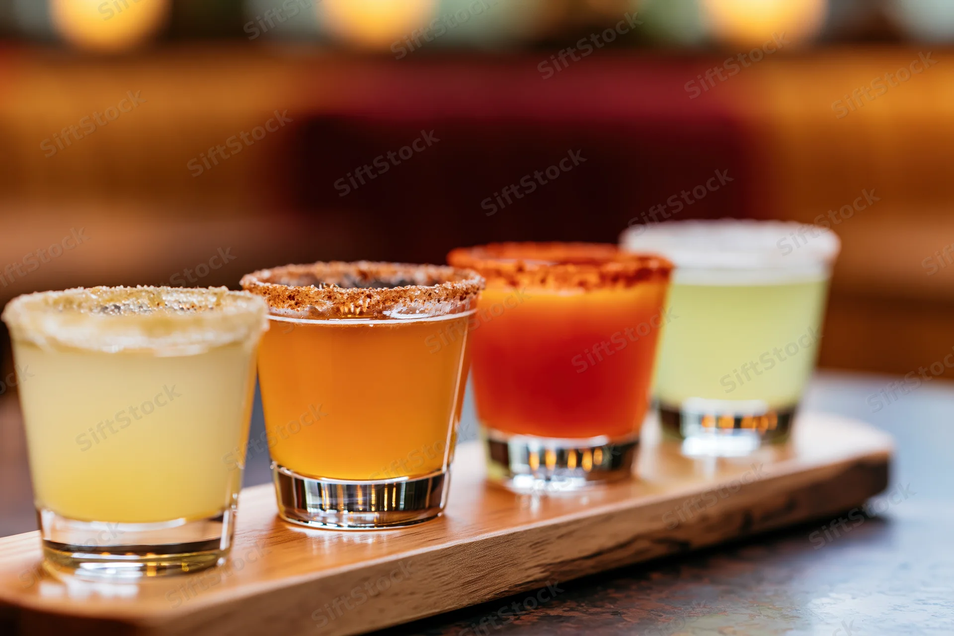 Four margarita flight glasses arranged in a row on a wooden tray at a bar
