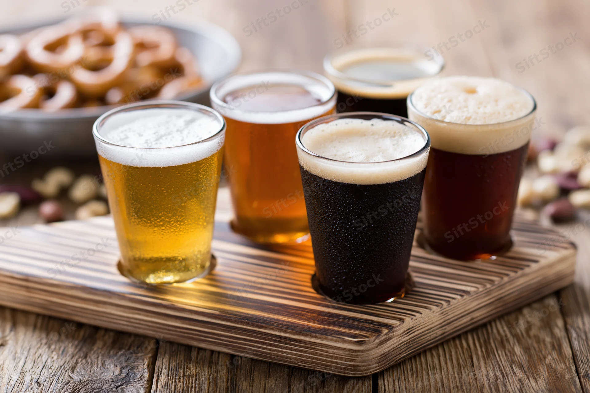 Four small tasting glasses of beer arranged in a row on a wooden tray with snacks nearby