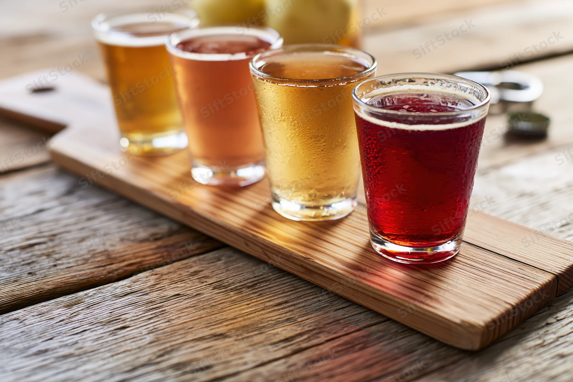 Four small glasses of cider arranged in a row on a wooden board