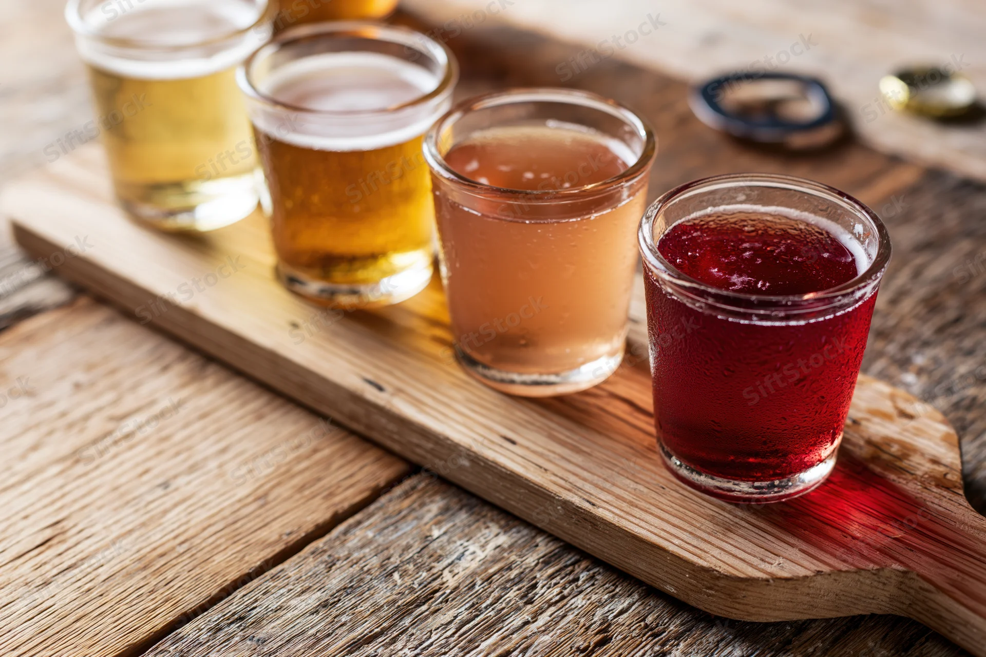 Four small glasses of cider arranged in a row on a wooden board