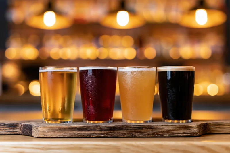 Four craft beer tasting glasses arranged in a row on a wooden tray at a bar