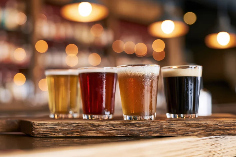 Four craft beer tasting glasses arranged in a row on a wooden tray at a bar