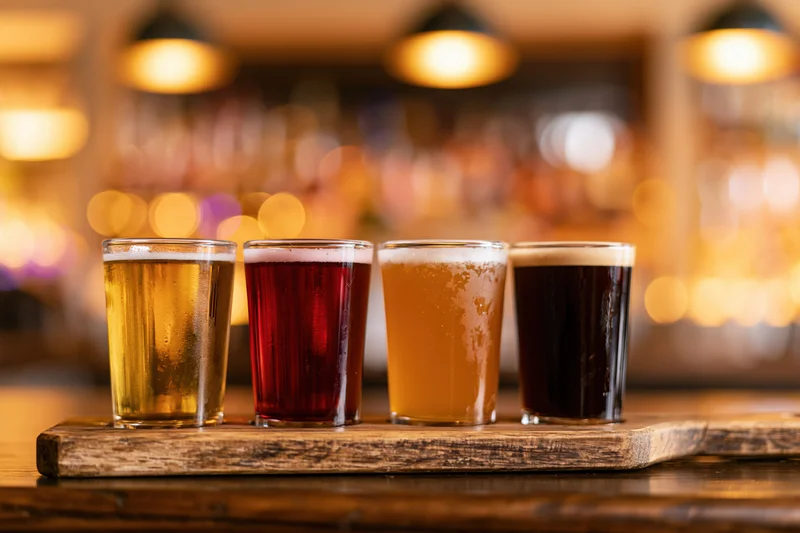 Four craft beer tasting glasses arranged in a row on a wooden tray at a bar