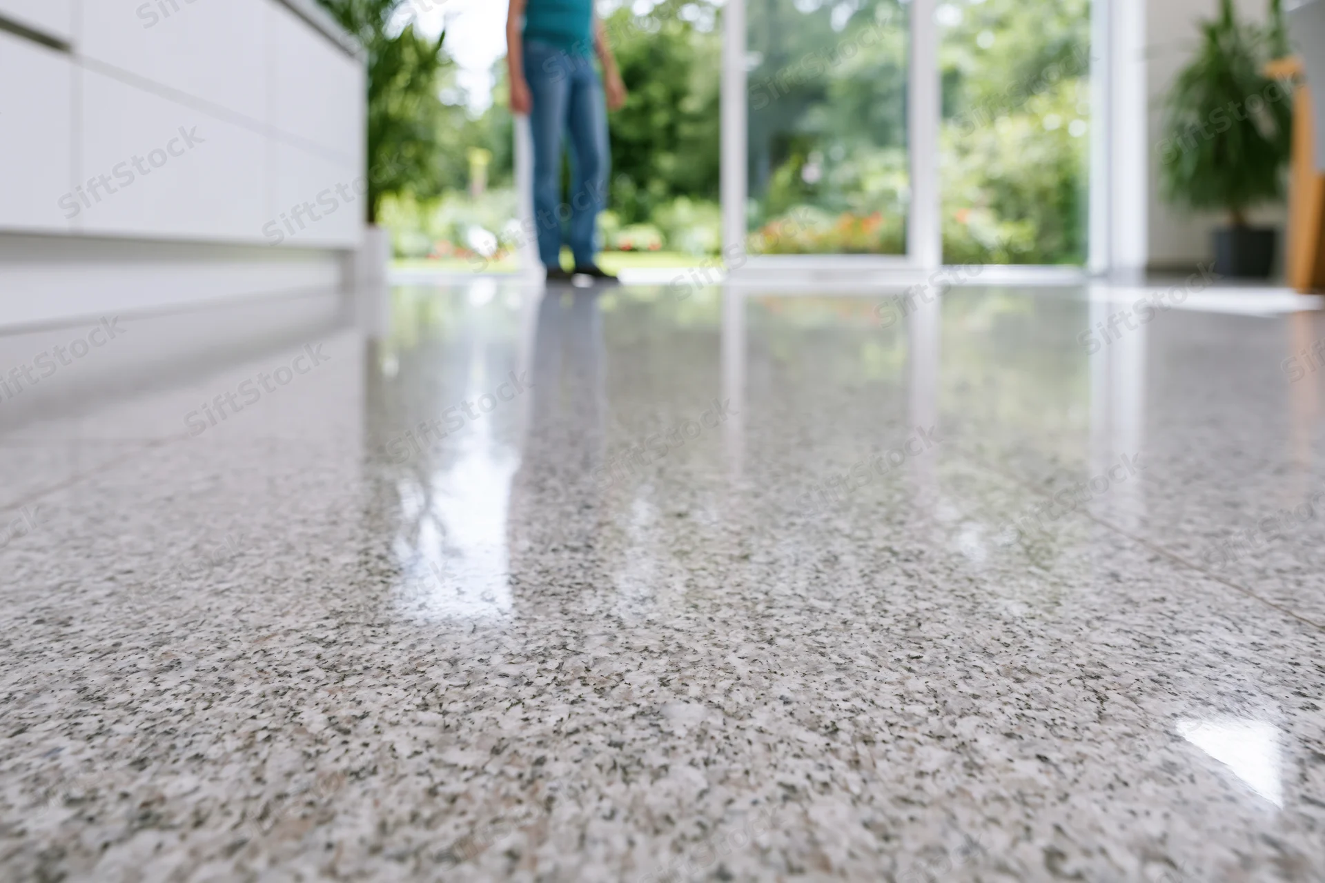 Polished granite floor in a modern home interior with a person standing near a glass door leading to a garden