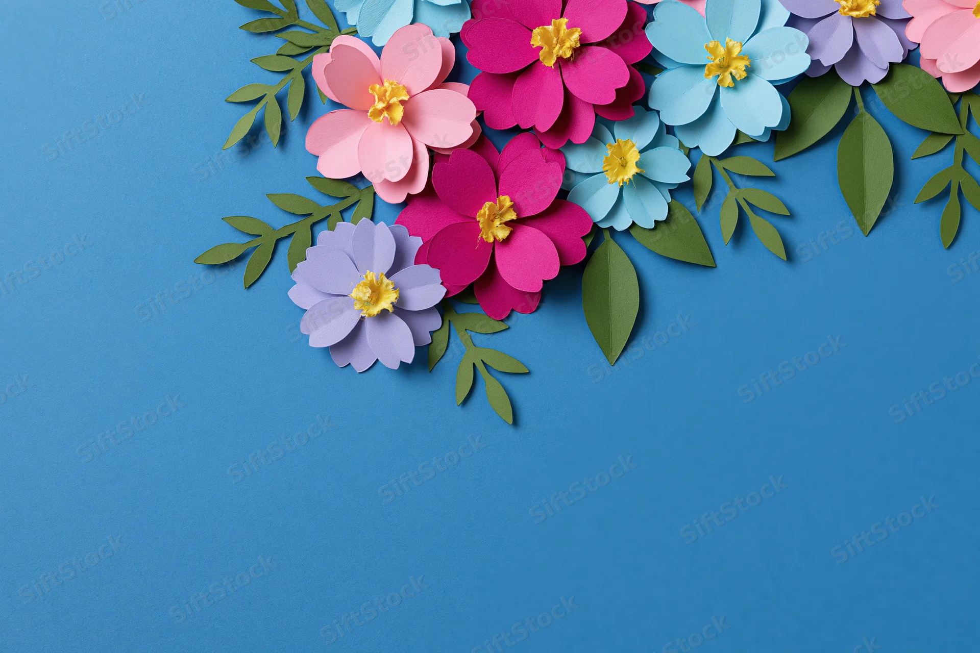 Handcrafted paper flowers and leaves arranged along the right side of a blue background