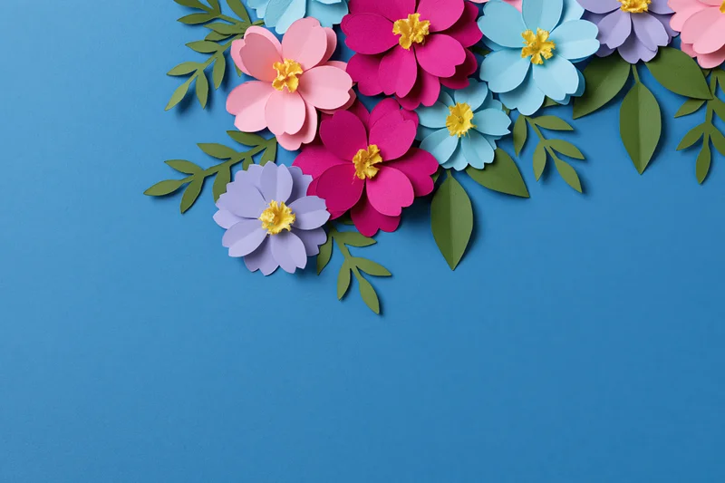 Handcrafted paper flowers and leaves arranged along the right side of a blue background