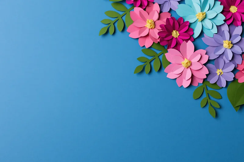 Handcrafted paper flowers and leaves arranged along the right side of a blue background
