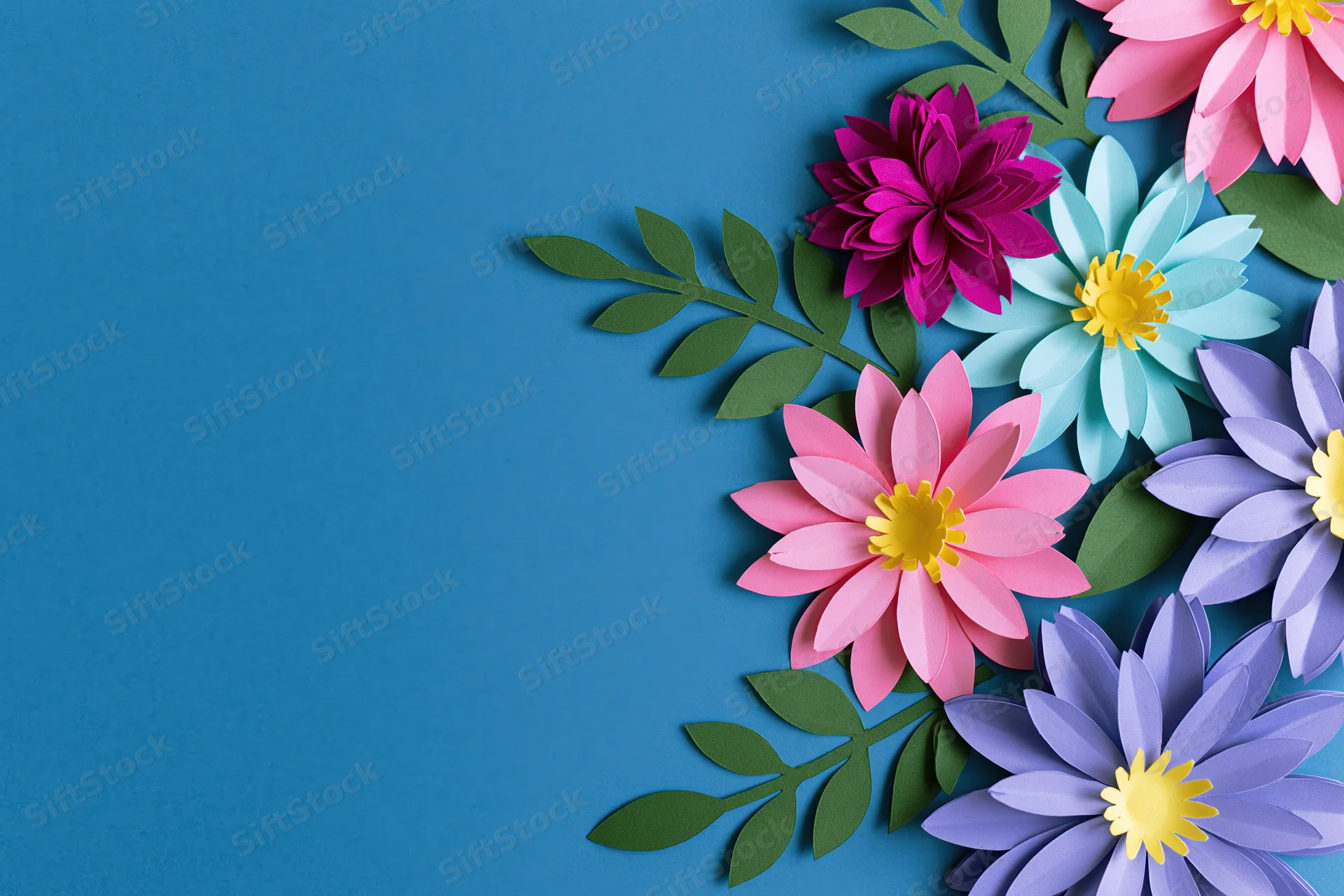 Handcrafted paper flowers and leaves arranged along the right side of a blue background