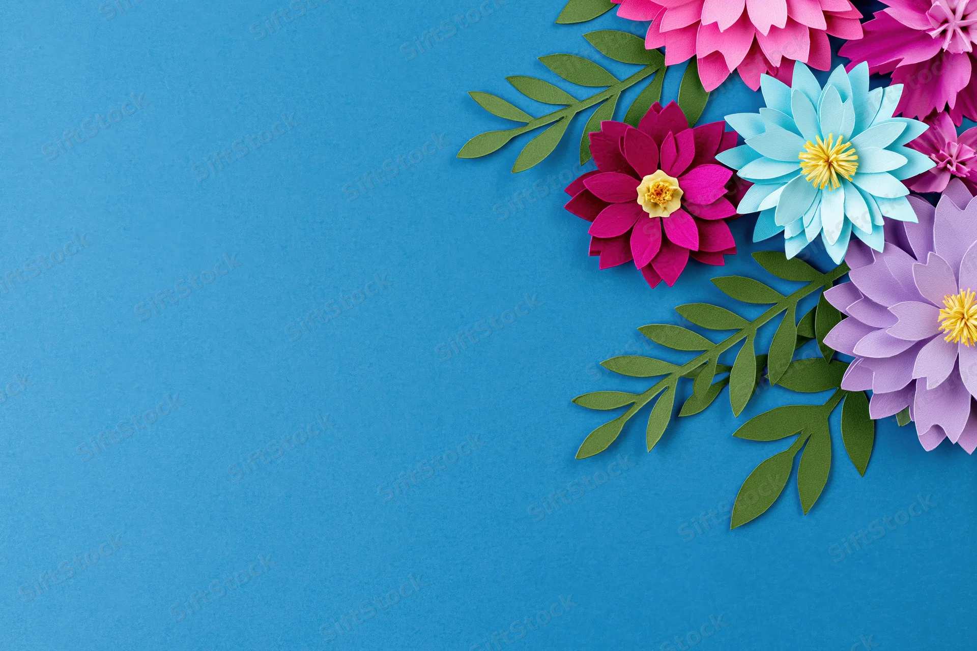 Handcrafted paper flowers and leaves arranged along the right side of a blue background