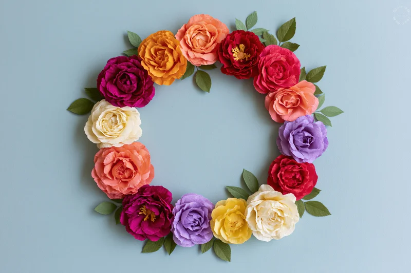 Handmade crepe paper flowers arranged in an oval wreath frame on a light blue background