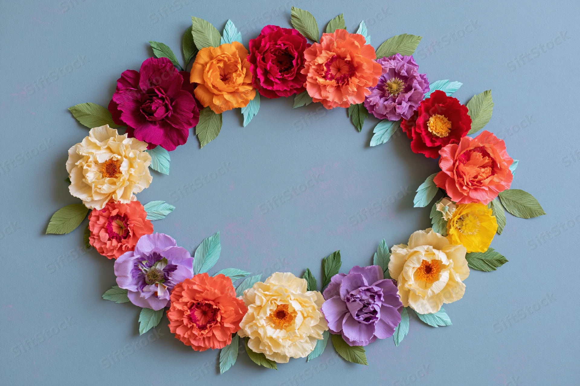 Handmade crepe paper flowers arranged in an oval wreath frame on a plain background