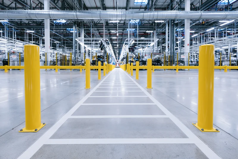 Empty automotive assembly line in a modern factory interior with yellow safety bollards and white floor markings