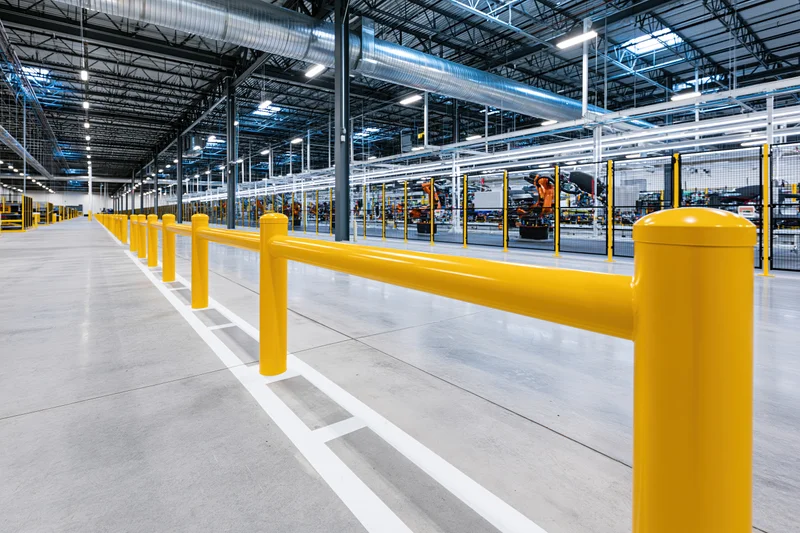 Empty automotive manufacturing plant interior with yellow safety barriers and robotic assembly line in background