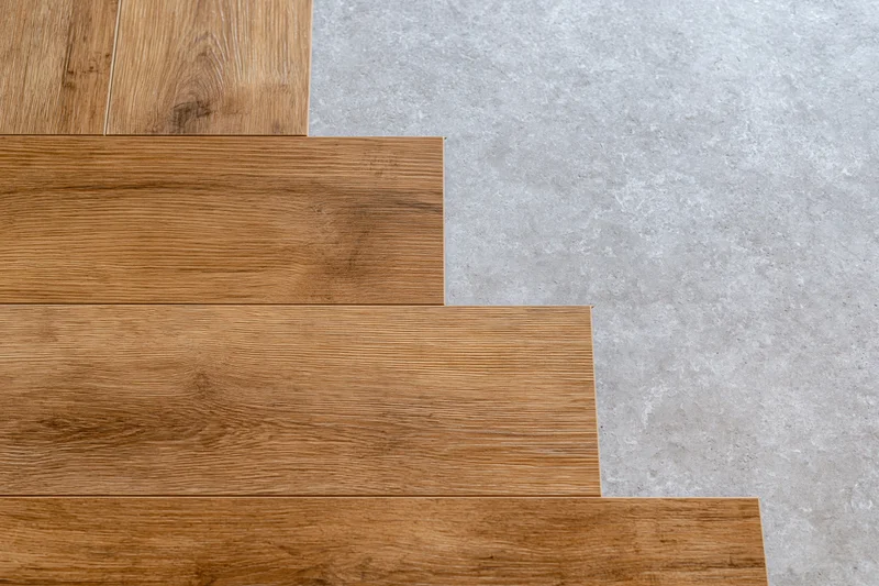 Laminate wood flooring planks laid in progress on concrete subfloor showing edge transition