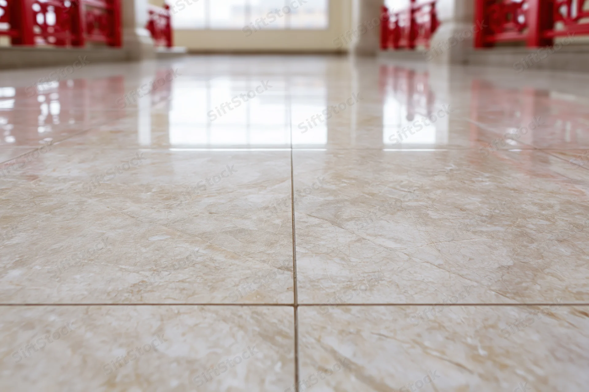 Polished marble tile floor filling the frame with reflective surface and red furniture in background