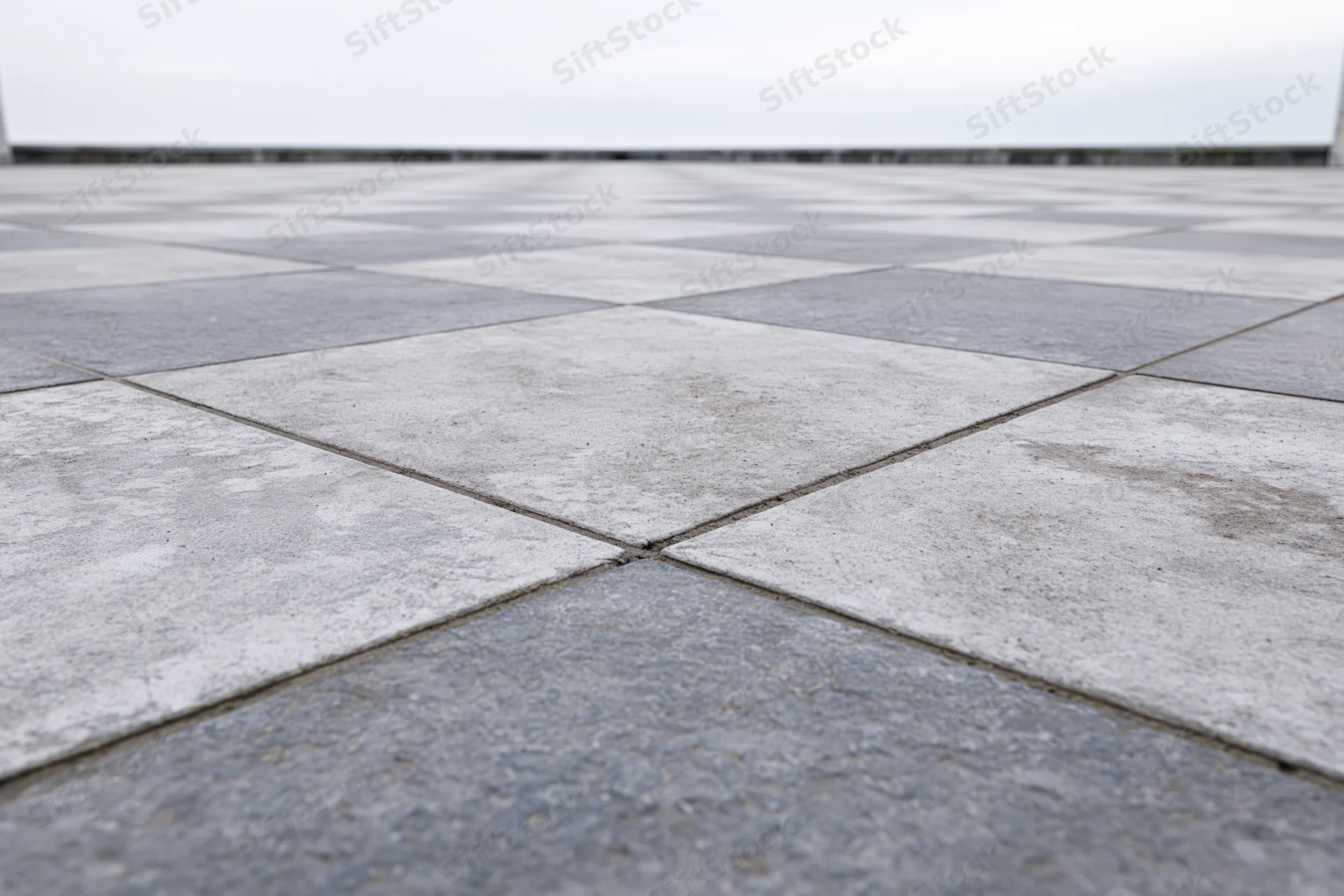 Square concrete paving tiles arranged in a grid pattern extending to a vanishing point on an outdoor ground surface