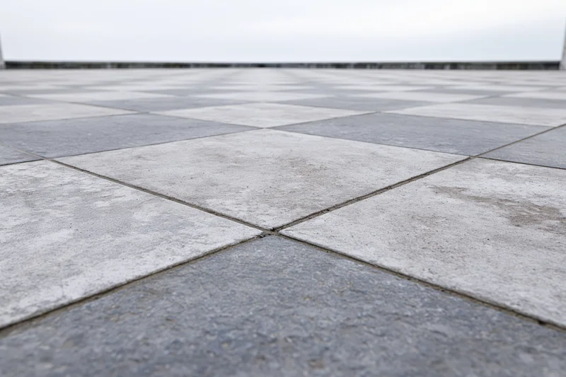 Square concrete paving tiles arranged in a grid pattern extending to a vanishing point on an outdoor ground surface