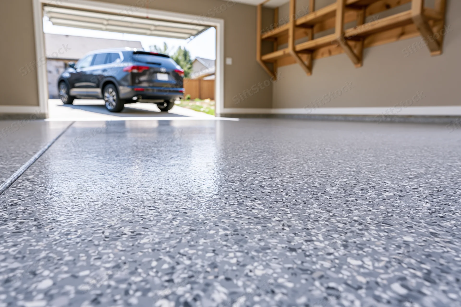 Low-angle view of epoxy-coated garage floor with black SUV parked outside through open door