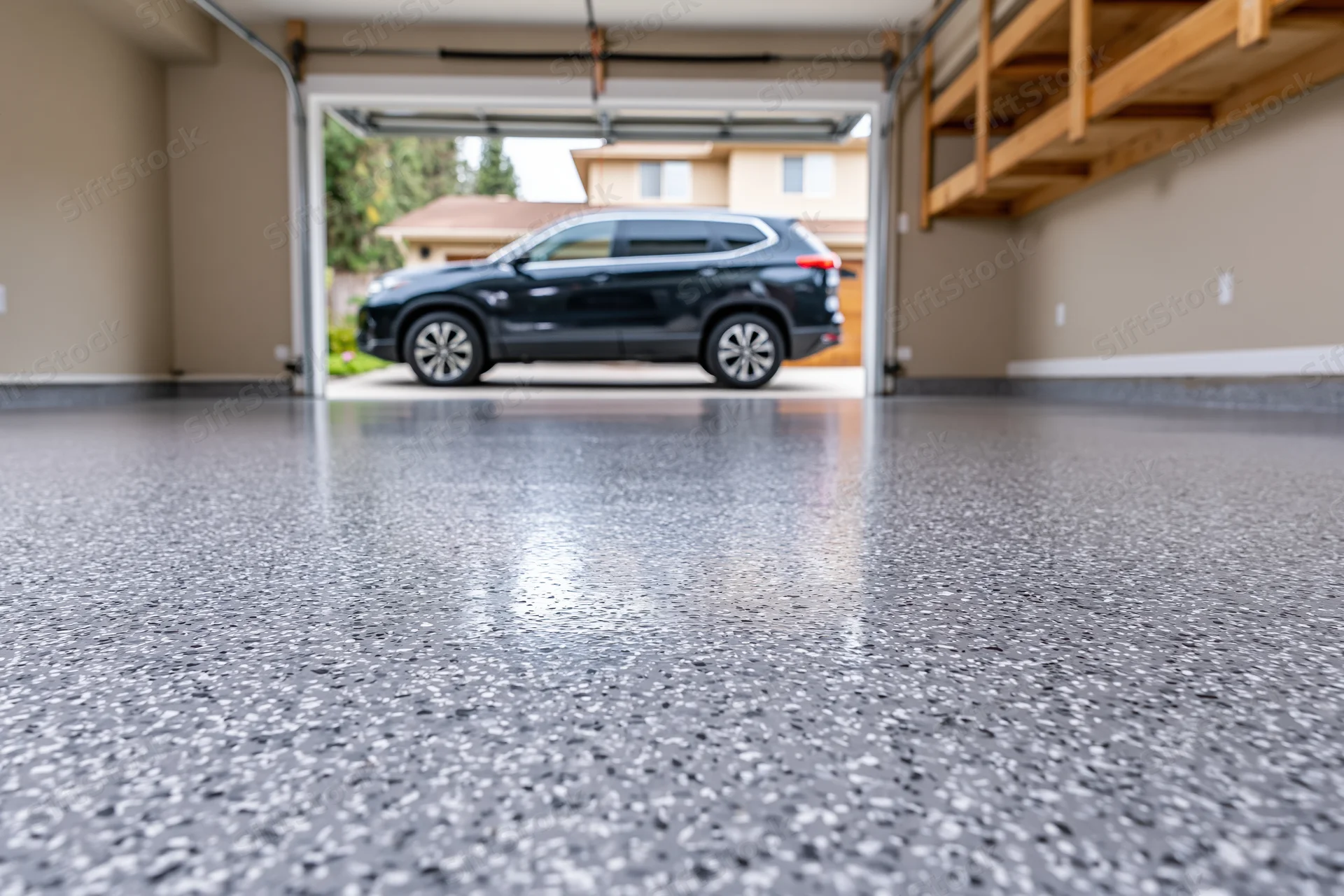 Low-angle view of a clean epoxy-coated garage floor with a black SUV parked outside the open door