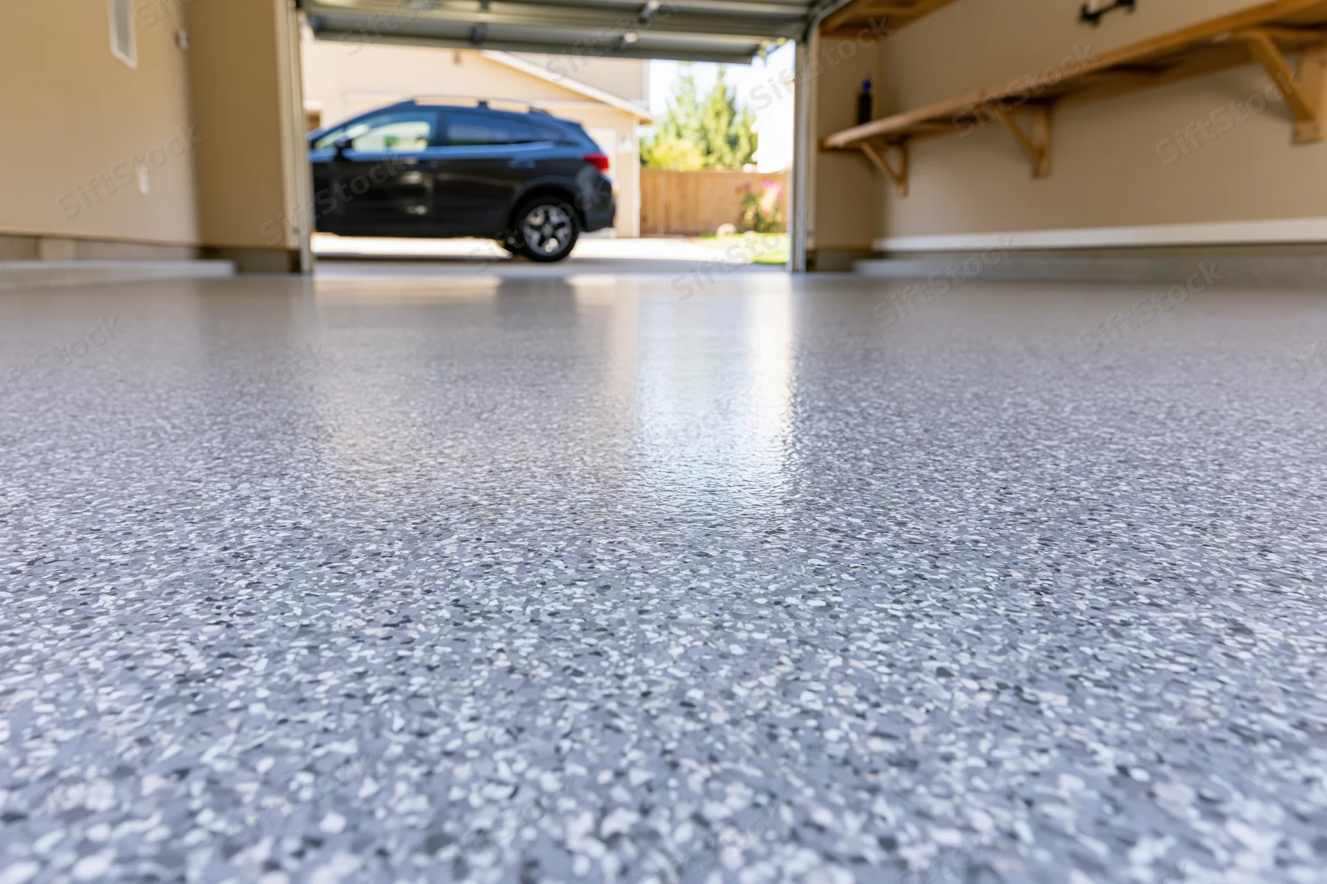 Low-angle view of a clean epoxy-coated garage floor with a black SUV parked outside the open door