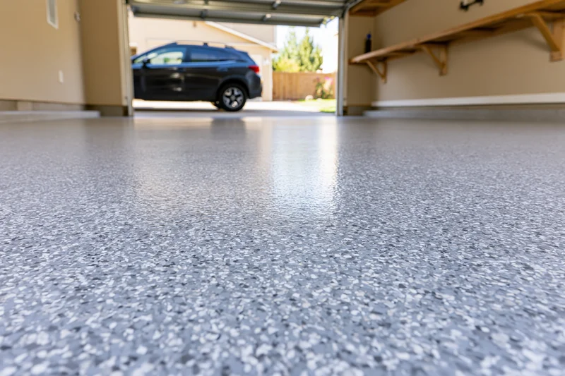 Low-angle view of a clean epoxy-coated garage floor with a black SUV parked outside the open door