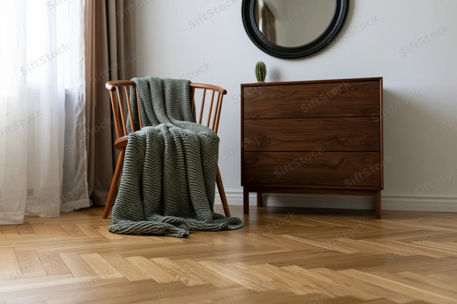 Wooden armchair draped in green knitted blanket beside dresser in minimalist bedroom corner