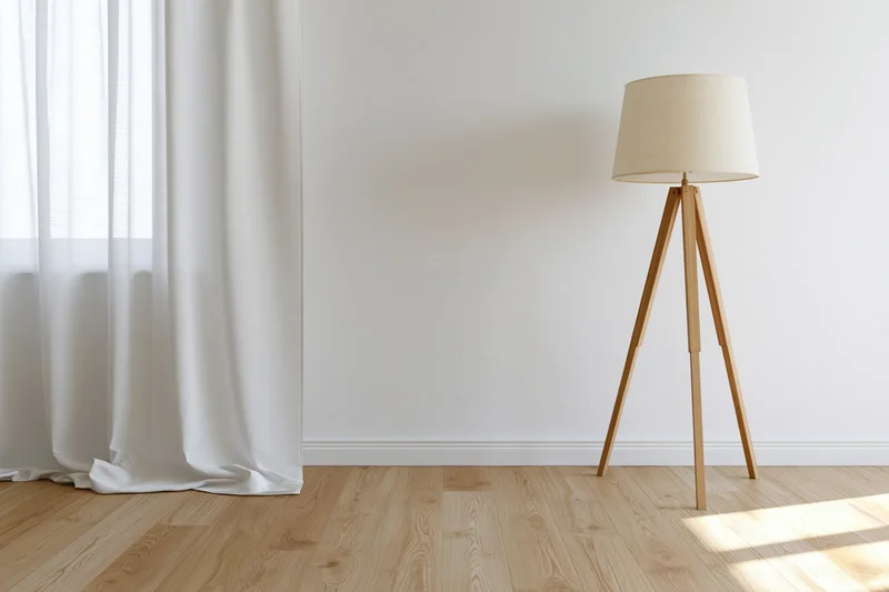 Wooden tripod floor lamp in minimalist empty room with white curtain and hardwood flooring