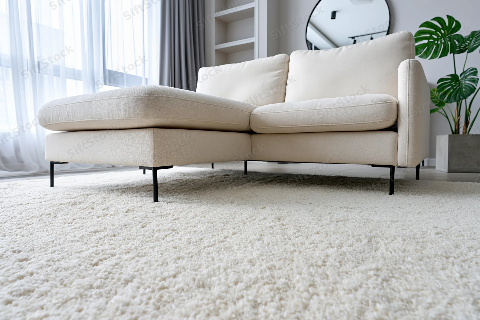 Cream sofa with chaise lounge on white rug in minimalist living room with window and plant