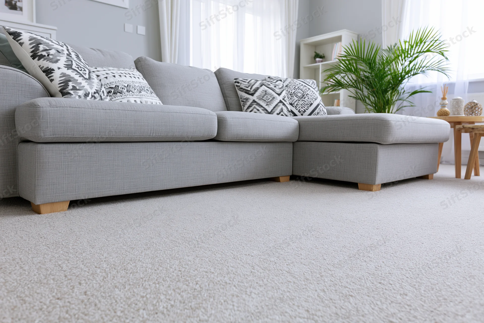 Low-angle view of a gray sectional sofa with patterned throw pillows in a modern minimalist living room with natural light and greenery
