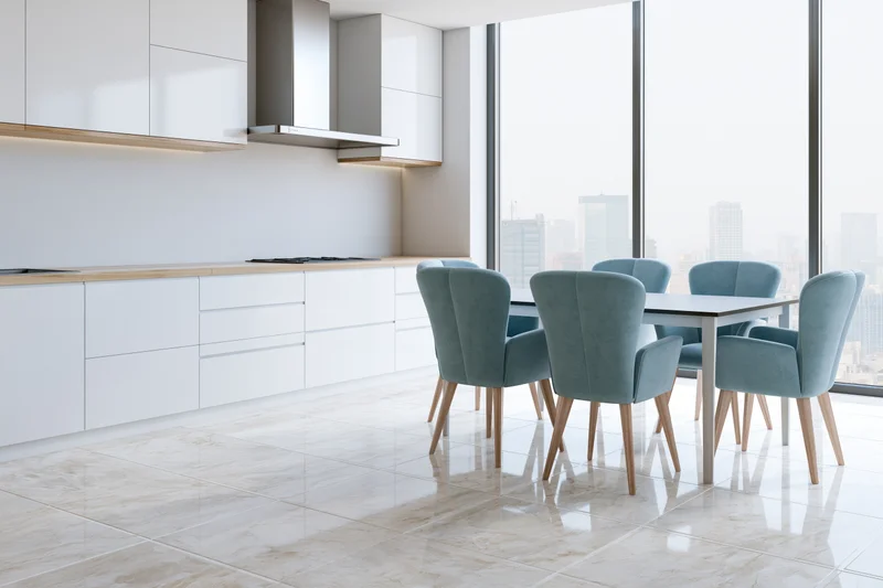 Modern open-plan kitchen and dining area with white cabinetry and teal chairs overlooking city from large windows