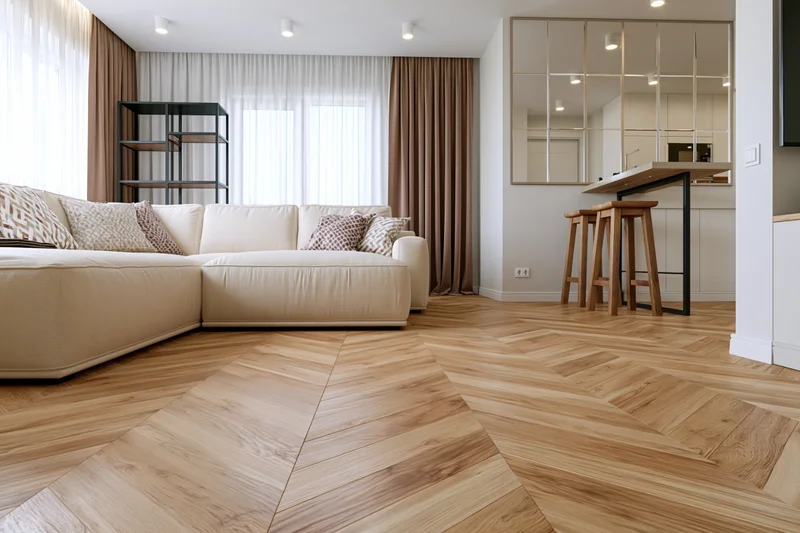 Modern open-plan living room with beige sectional sofa and herringbone wood flooring viewed from low angle