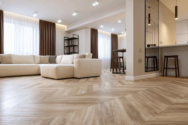Modern open-plan living room with beige sectional sofa and herringbone wood flooring viewed from low angle