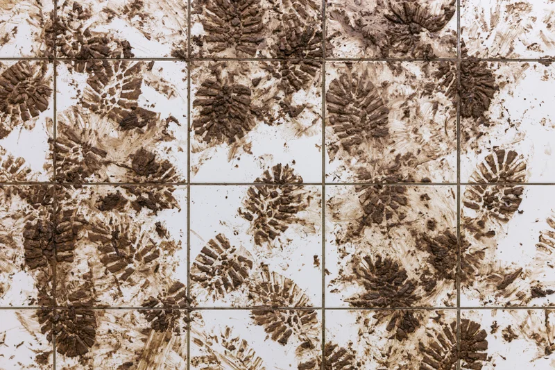 Muddy shoe prints and dirt smears scattered across white ceramic tiles in a grid pattern