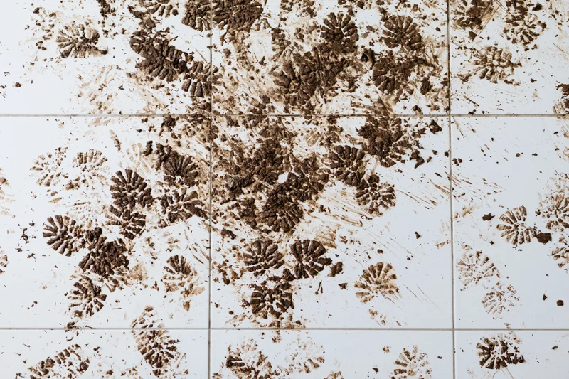 Muddy shoeprints and dirt smears scattered across white ceramic tile floor