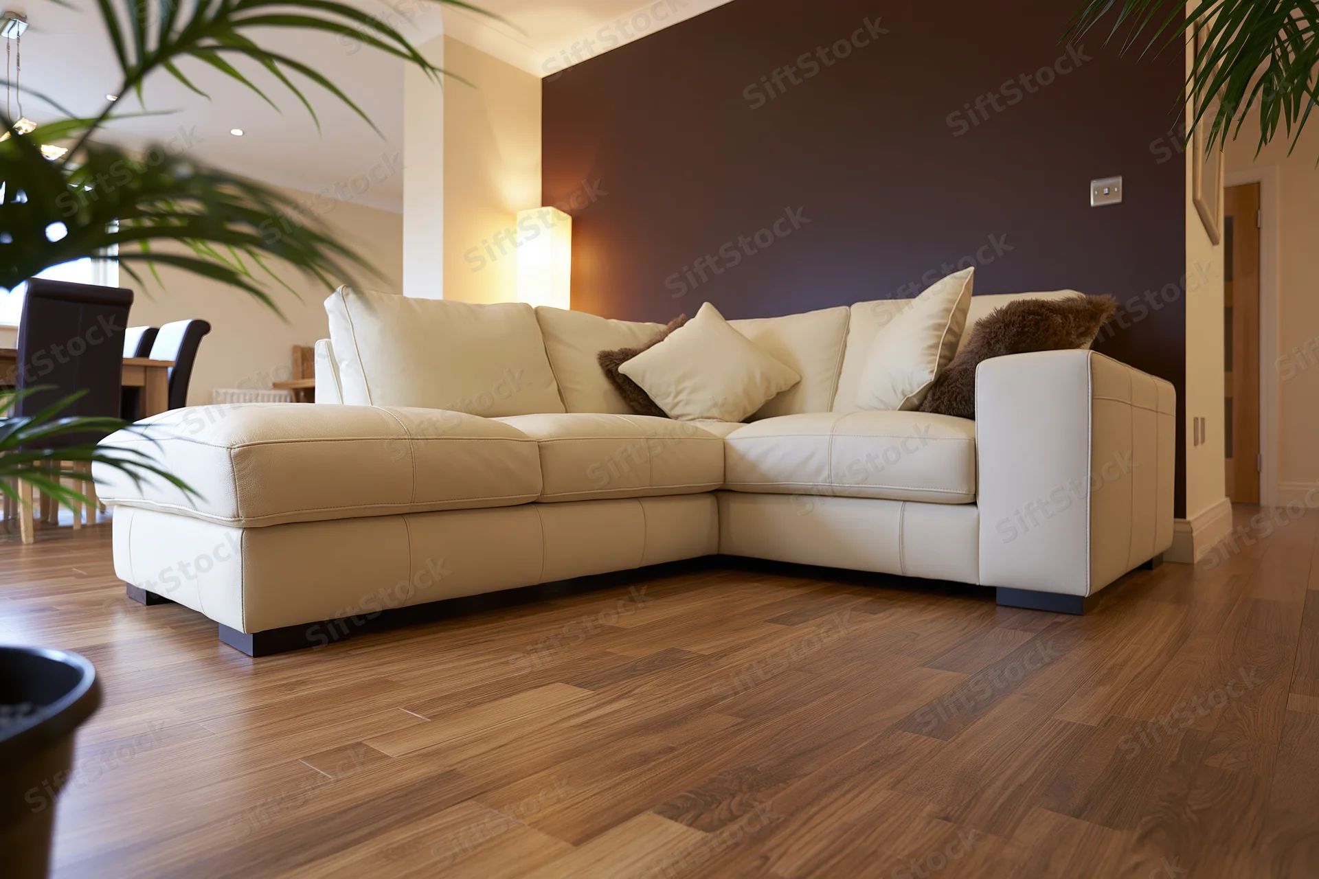 Beige leather sectional sofa in open-plan living and dining room with hardwood flooring and warm ambient lighting