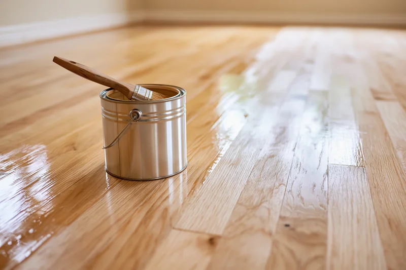 Metal paint can with brush resting inside on a freshly varnished hardwood floor