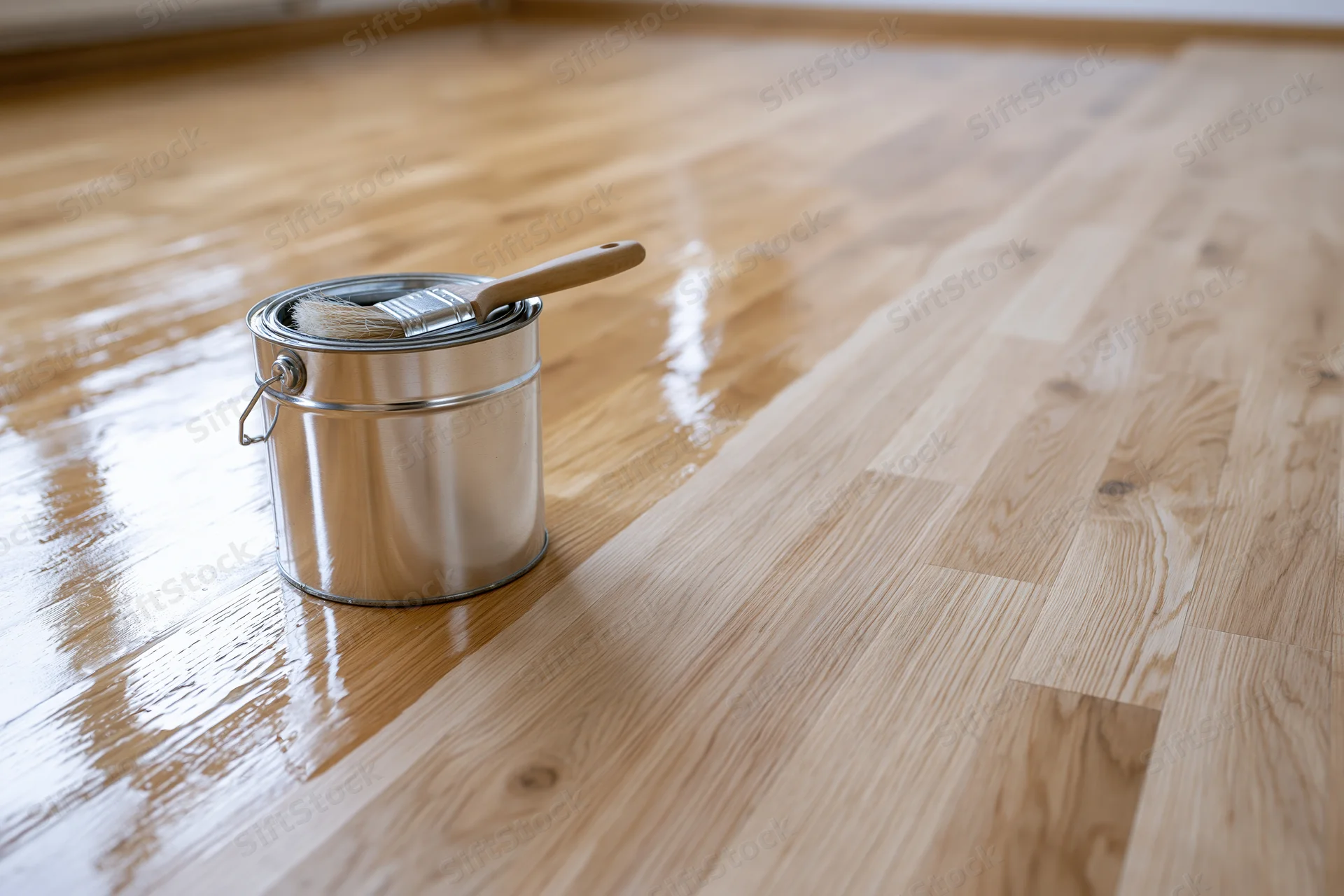 Metal paint can with brush resting inside on a freshly varnished hardwood floor