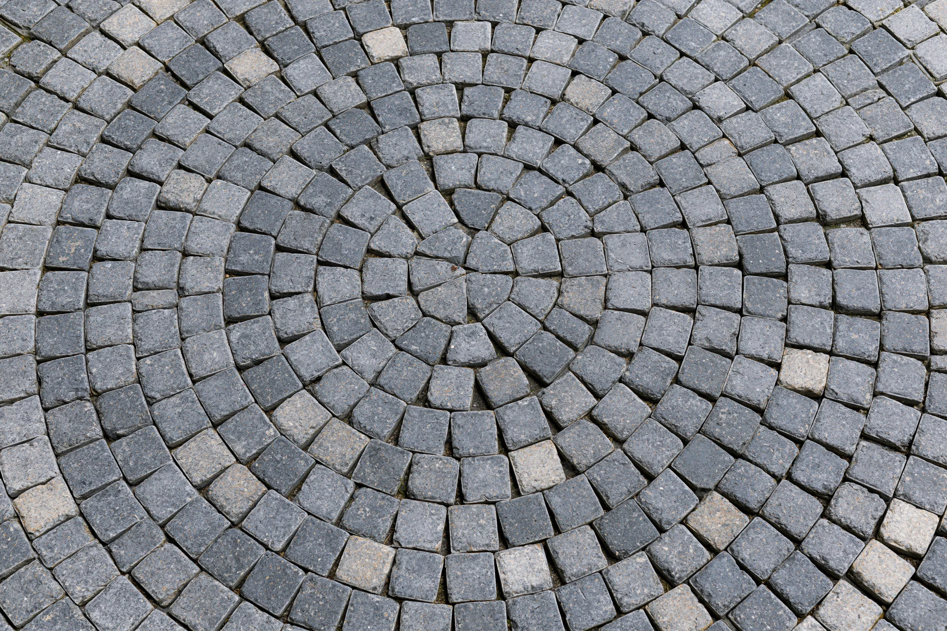 Circular grey cobblestone patio arranged in concentric rings with radial pattern on outdoor ground surface