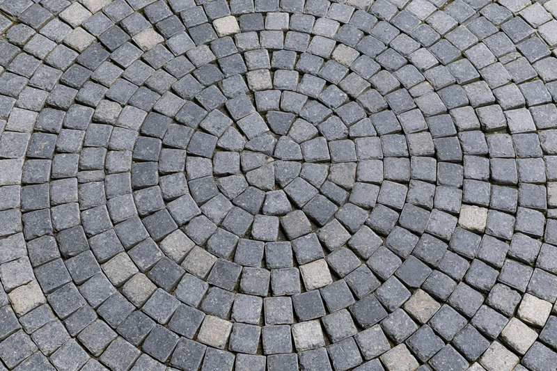 Circular grey cobblestone patio arranged in concentric rings with radial pattern on outdoor ground surface
