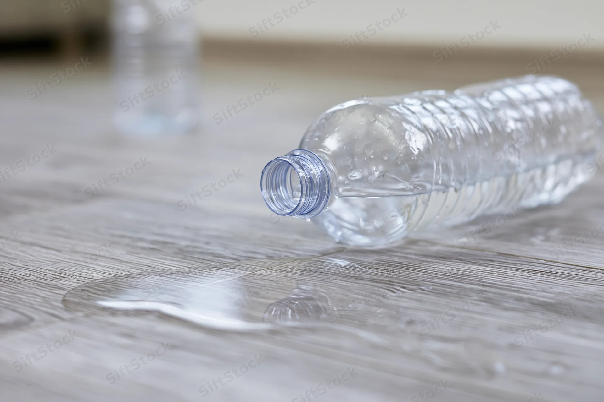 Overturned clear plastic water bottle lying on its side with spilled liquid on wooden floor