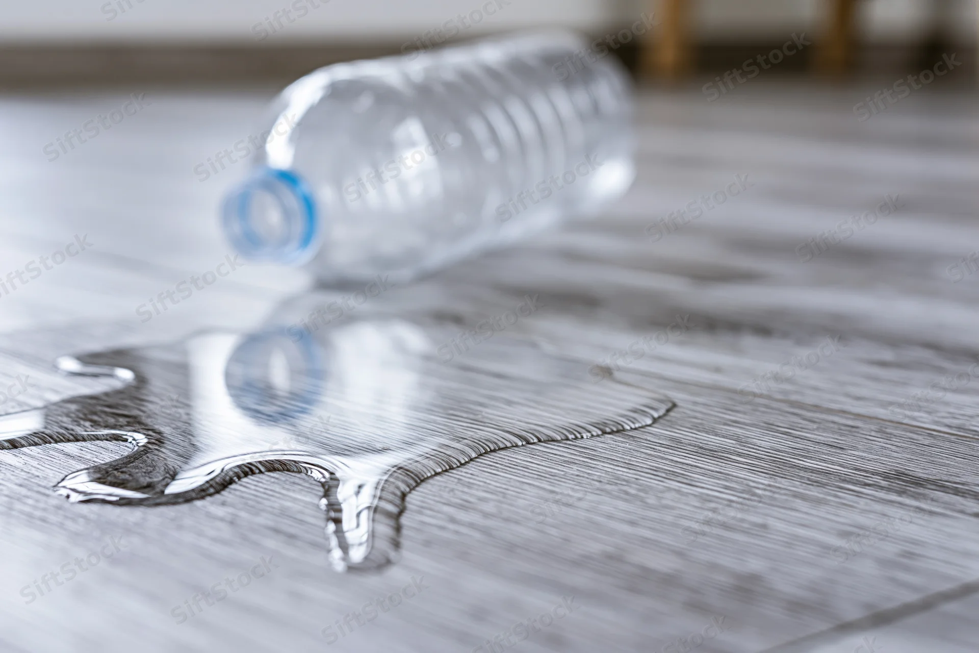 Overturned plastic water bottle lying on its side with spilled liquid on laminate floor