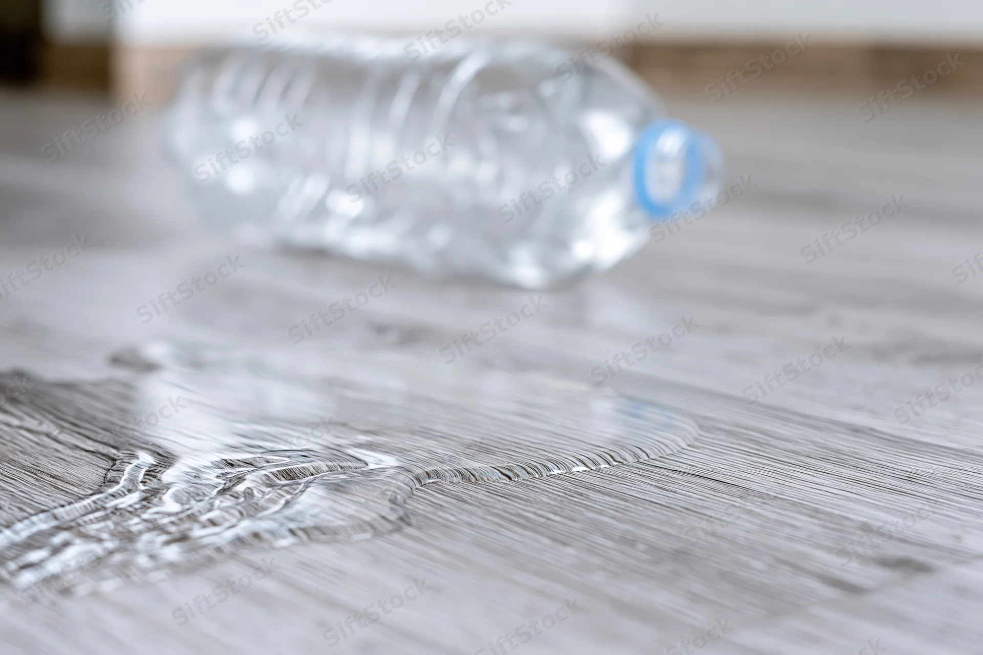 Overturned plastic water bottle lying on wooden floor with spilled liquid forming puddle