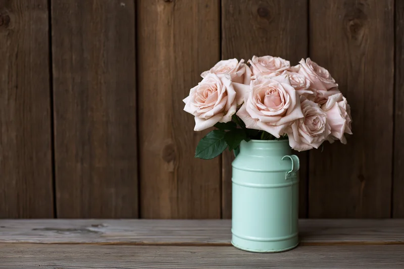 Blush roses arranged in a vintage mint-green metal milk can on a wooden surface