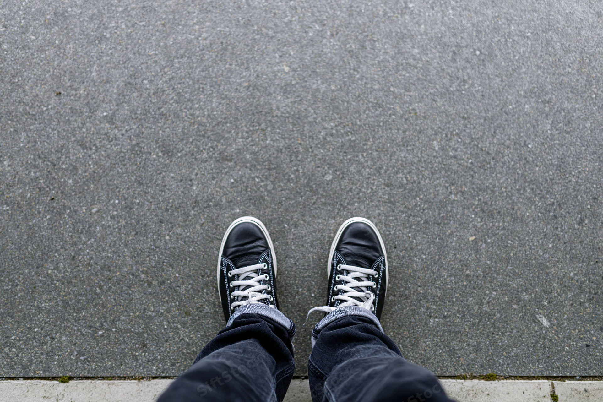 Person standing on concrete pavement wearing black sneakers and jeans