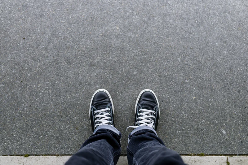 Person standing on concrete pavement wearing black sneakers and jeans