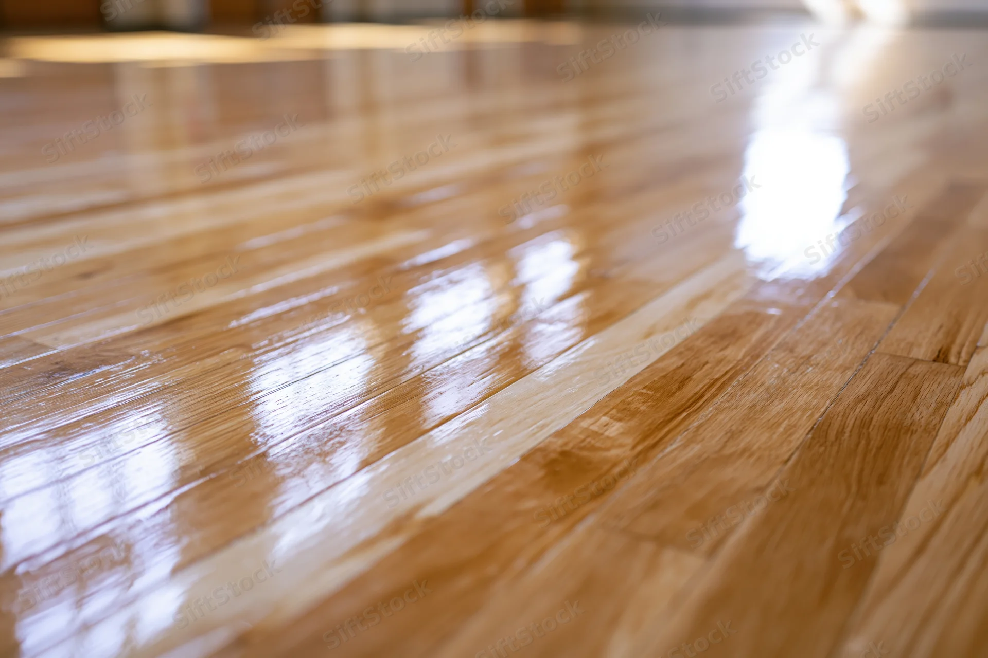 Polished hardwood gymnasium floor stretching into the distance with reflective surface and wood grain texture